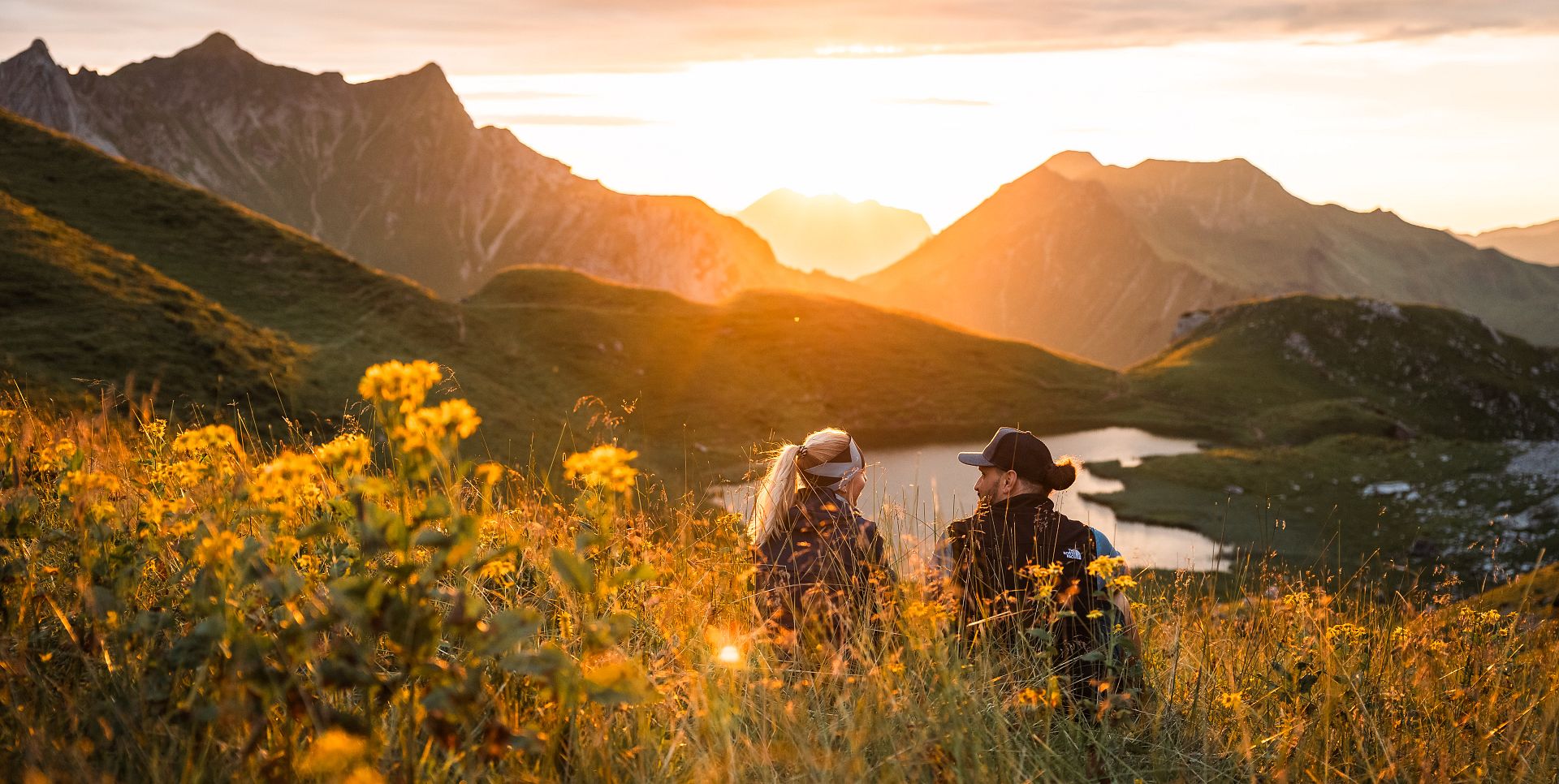 Two people are sitting by the Hochalpsee, admiring the sunset.