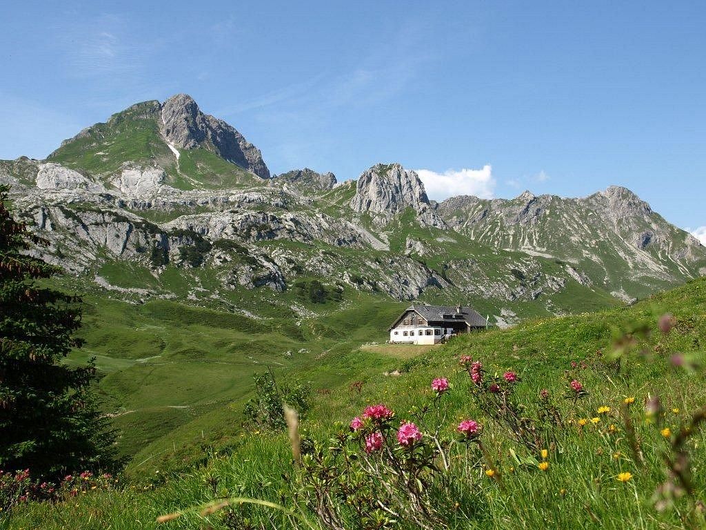 The Biberacher Hut is nestled in a green landscape, with mountains rising in the background.