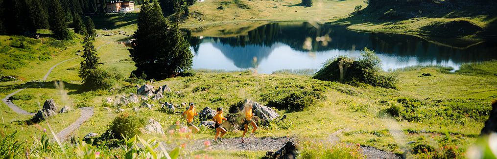 A close-up of three trail runners in yellow shirts running along the shore of Lake Körbersee.