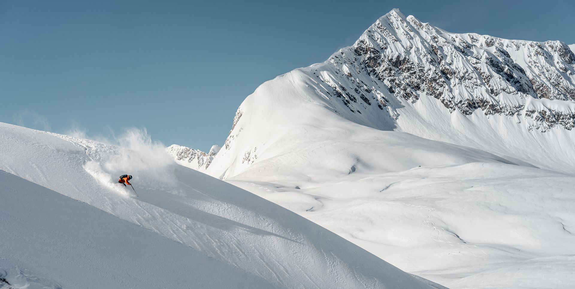 Freerider Martin Winkler rides through the powder snow, with snow-covered mountains rising in the background.