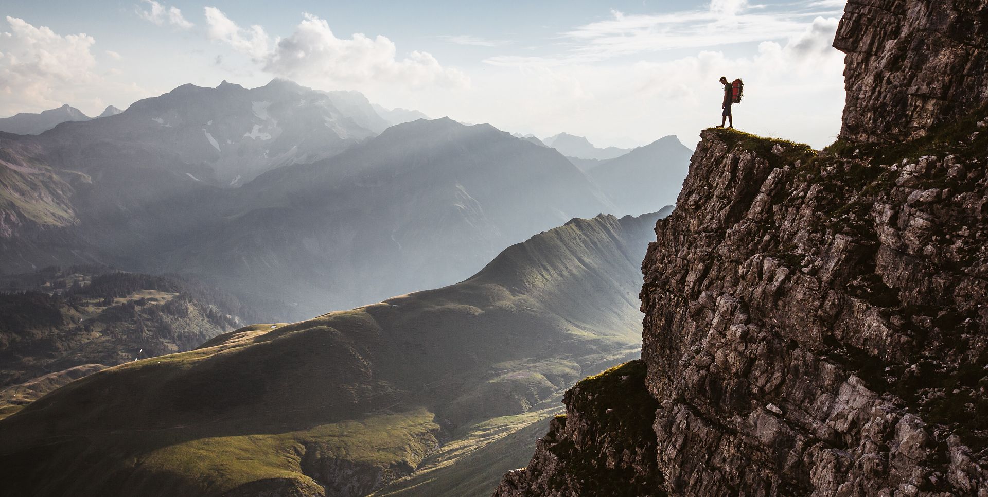 From a rock ledge, a man gazes down into the valley, with the mountain range and Kalbelsee unfolding before him.