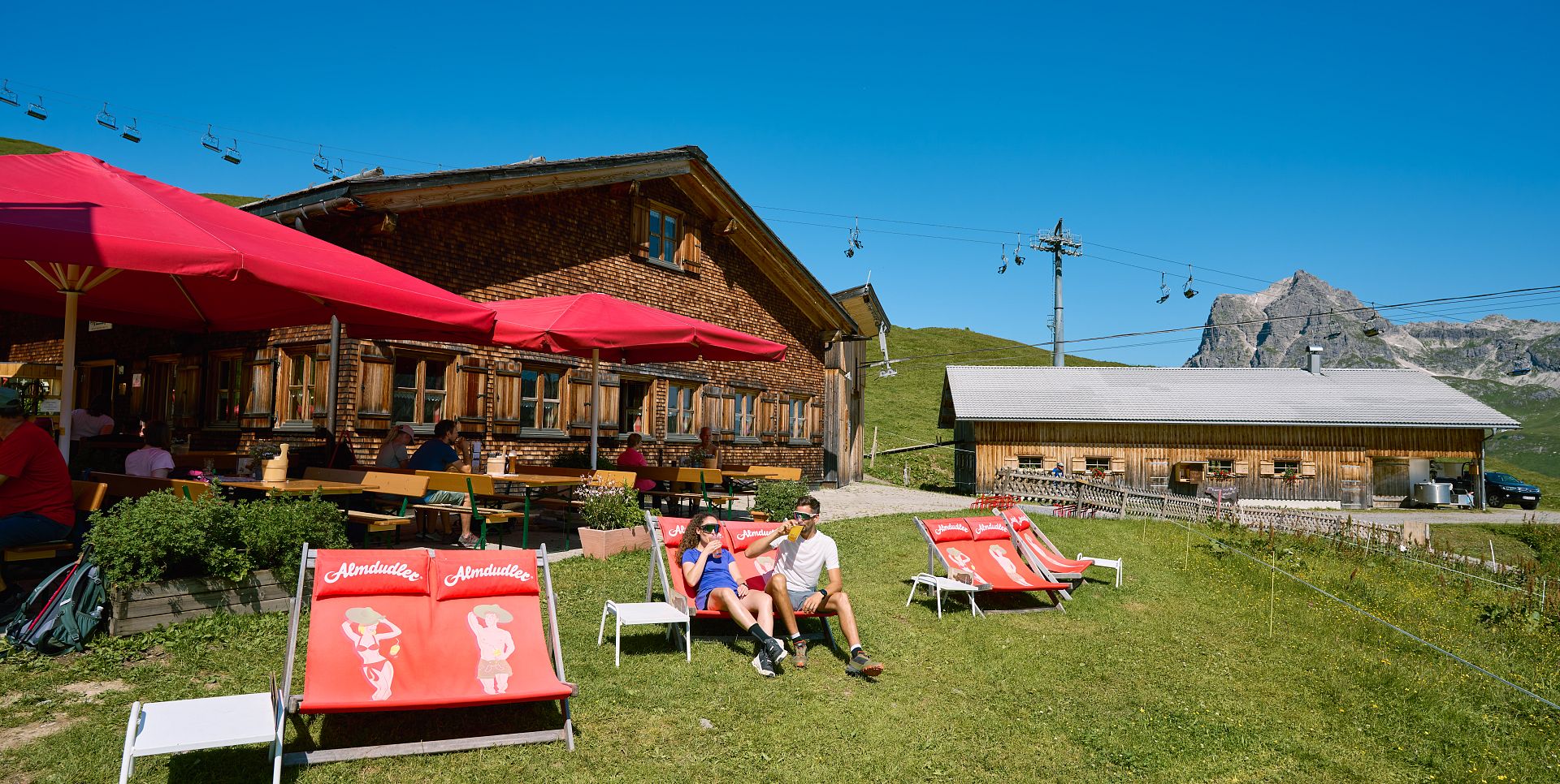 The sun terrace of the Hochalphütte is furnished with red parasols and deck chairs.