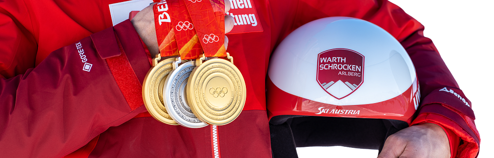 Johannes Strolz hält in einer Hand seine drei Olympiamedaillen und in der anderen seinen Skihelm mit dem Warth-Schröcken-Logo.