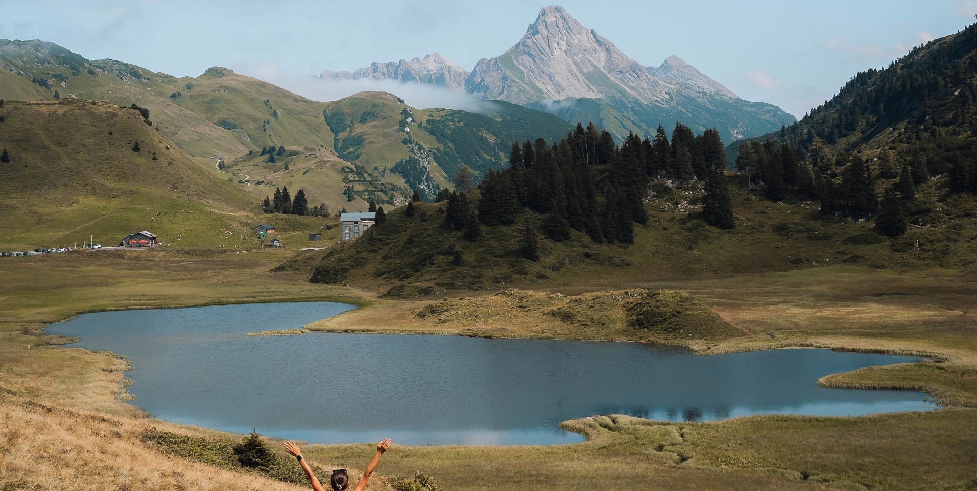 A lady stands on the shore of Lake Kalbele, gazing at the Biberkopf. The autumnal landscape unfolds around her in a colorful display.