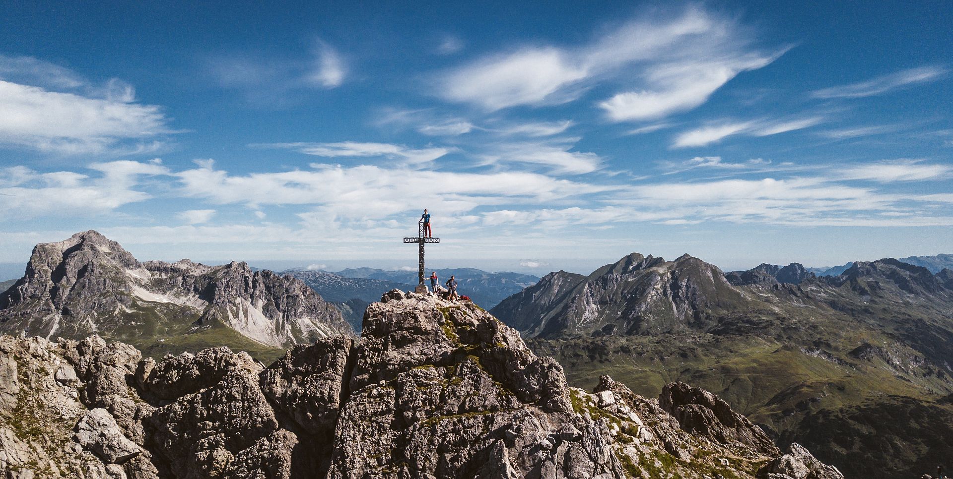 At the summit of Karhorn, three people stand with the impressive backdrop of the Allgäu Alps stretching out behind them.