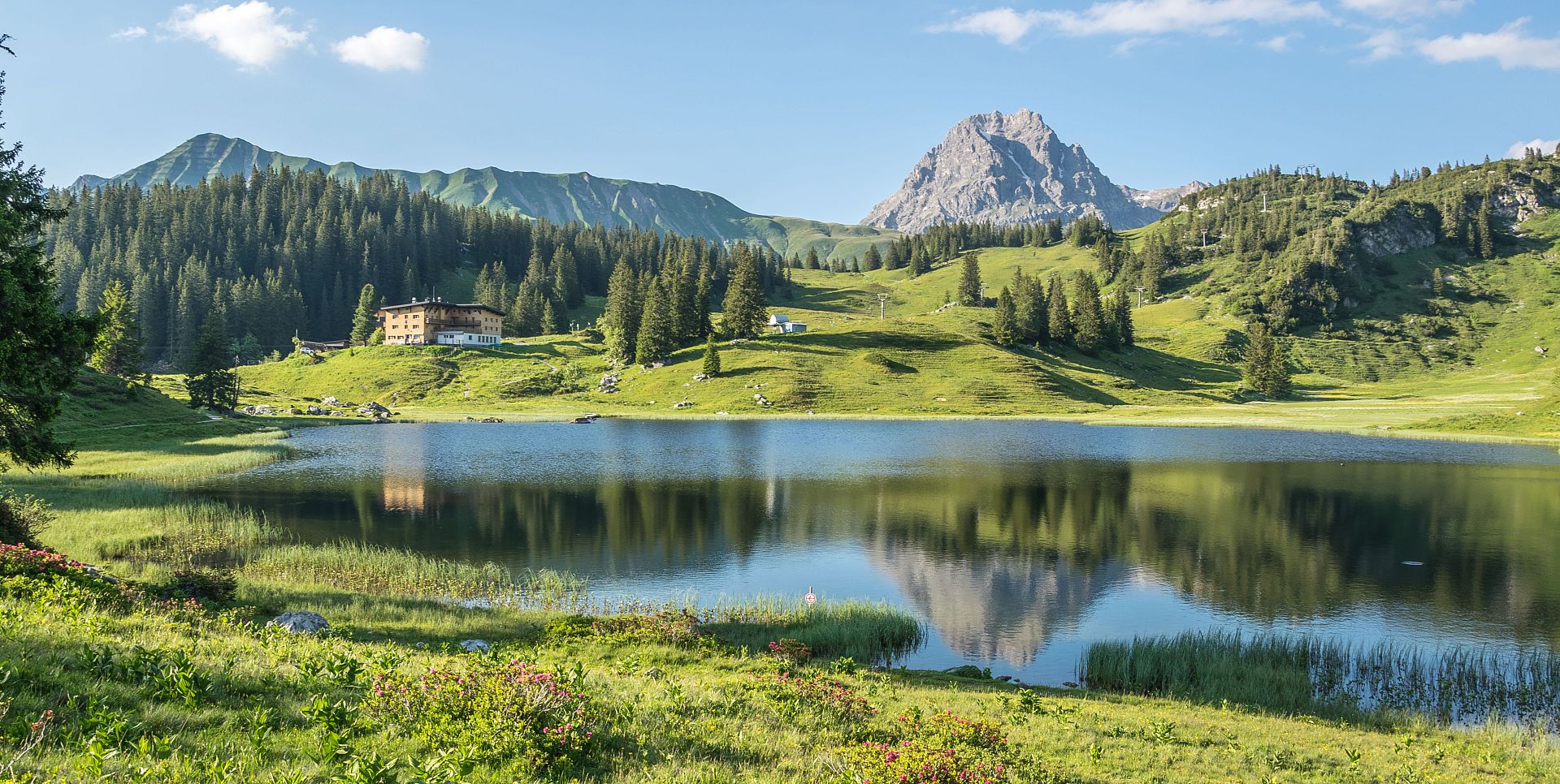 Am glitzernden Körbersee liegt das Berghotel, dahinter erheben sich die Höferspitze und der Widderstein.