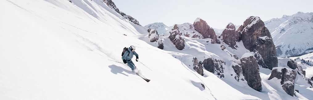 A skier makes their way down through the spring snow into Auenfeld in the morning, the sun on their face.