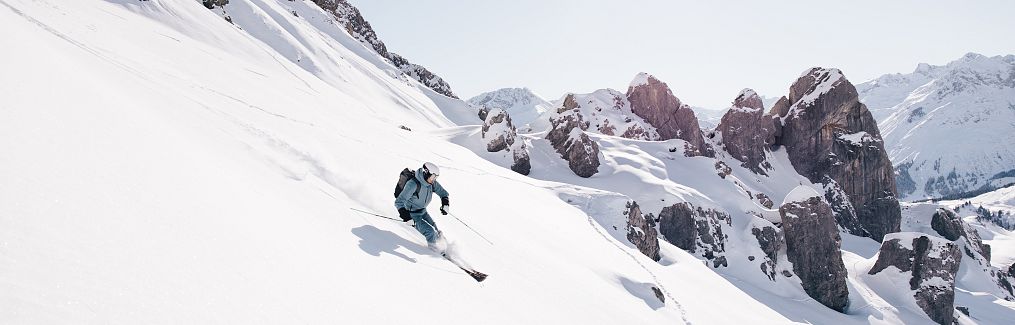 Ein Skifahrer zieht am Morgen durch den Firn hinab ins Auenfeld, die Sonne im Gesicht.
