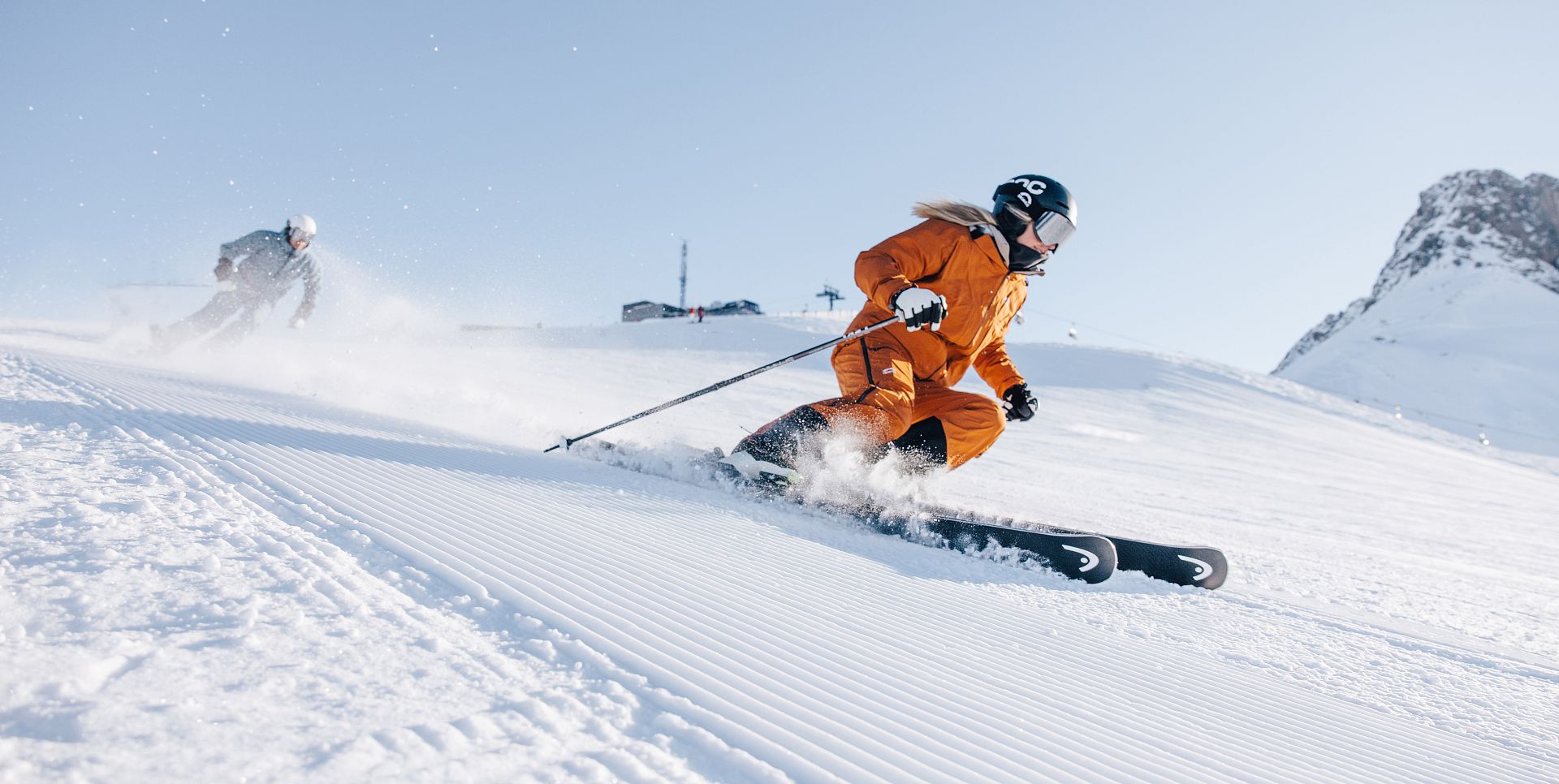 Two skiers glide down towards Auenfeld in the morning, the sun shining on their faces.