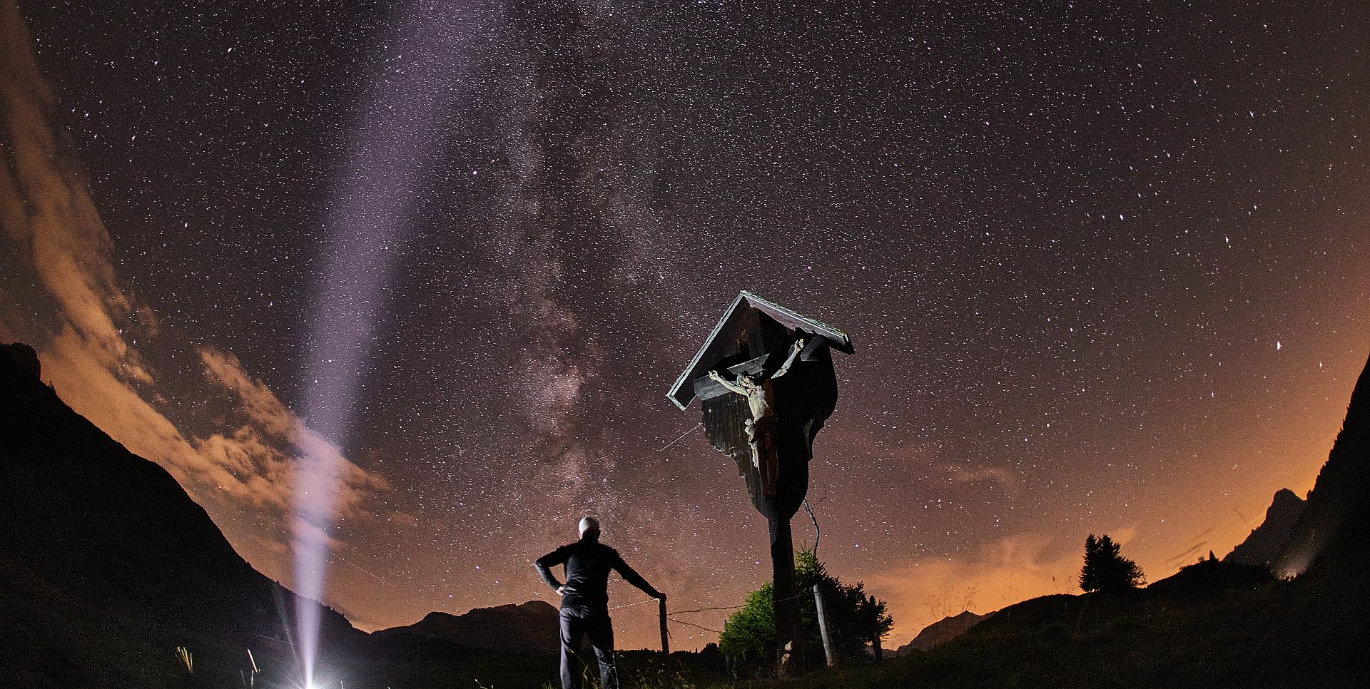 In front of the Körberkreuz, a man stands looking up at the sky, admiring the Milky Way.