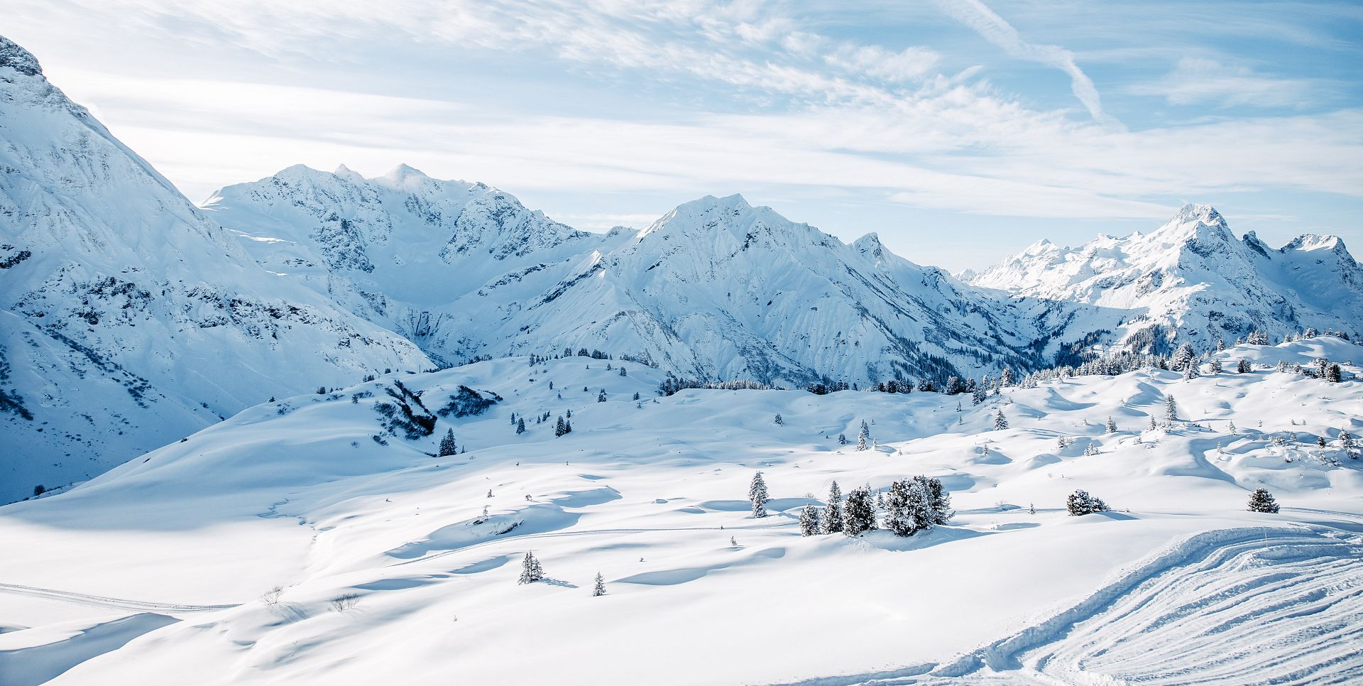 Verschneite Winterlandschaft mit schneebedeckten Bäumen und Bergen im Hintergrund.