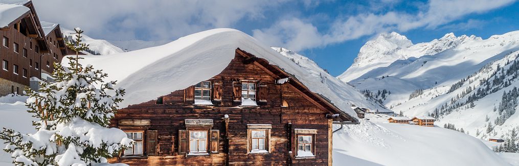 Ein altes Haus ruht in einer verschneiten Winterlandschaft, das Dach bedeckt von frischem Schnee.