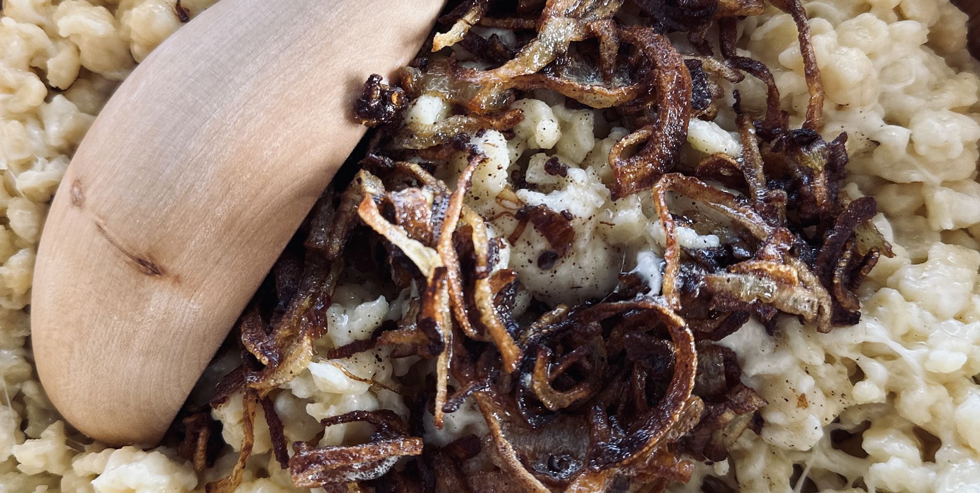Käsknöpfle mit gerösteten Zwiebeln, serviert mit einem Holzlöffel.