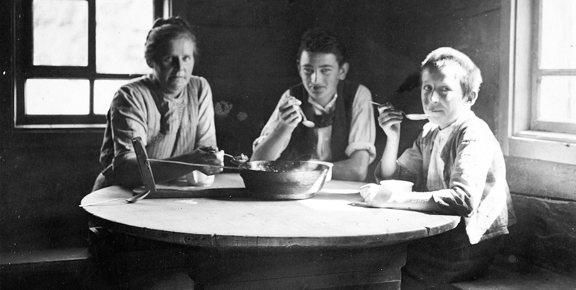 Old photo of three people sitting together at a table and eating.