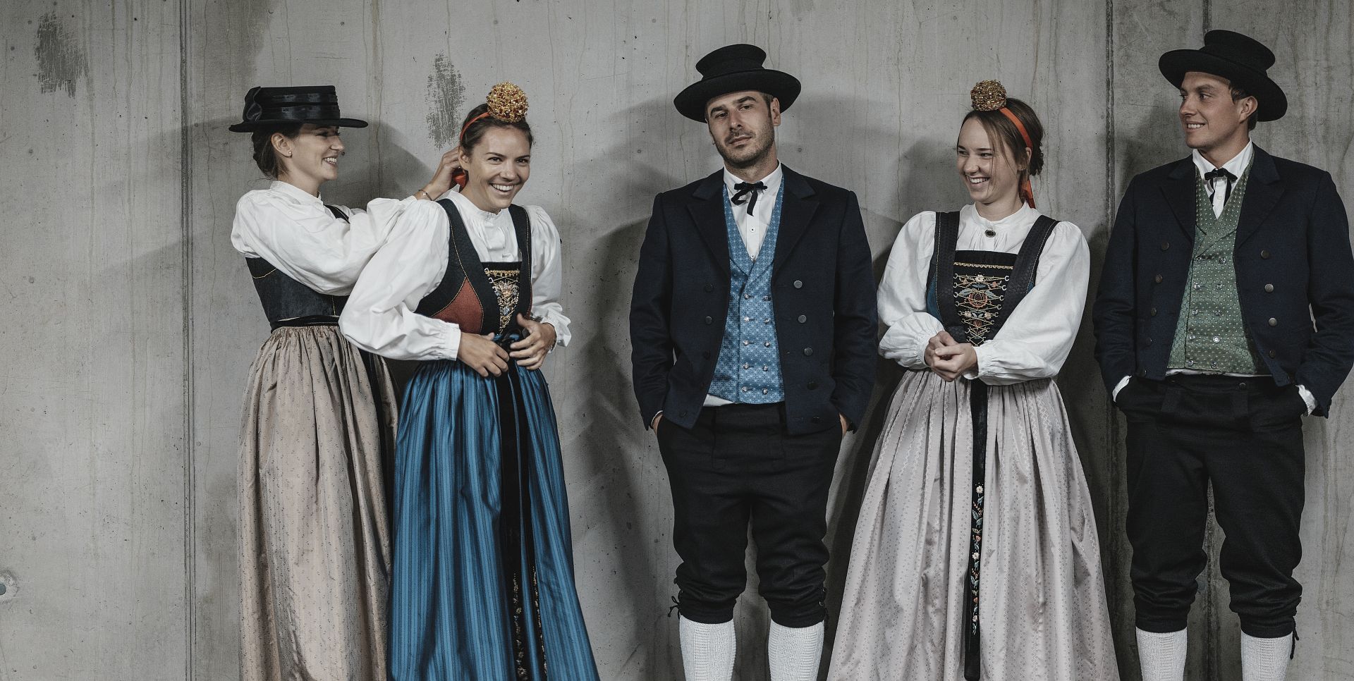 Damen und Herren in Walsertracht posieren vor einer Betonwand.