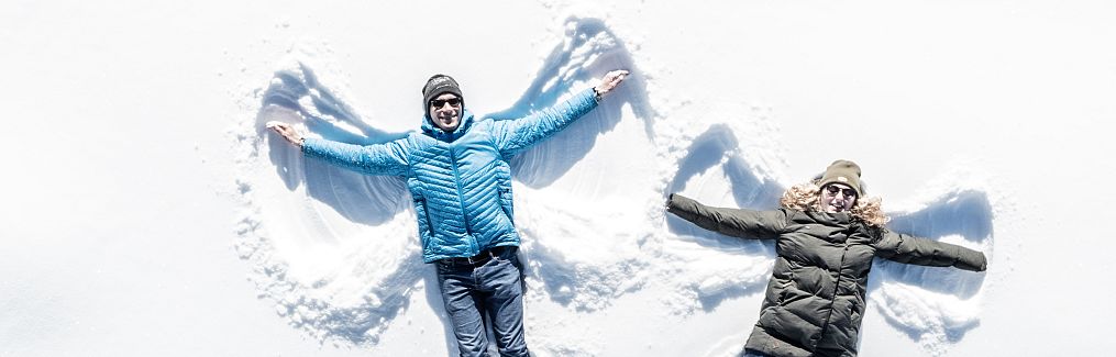 Ein Paar liegt nebeneinander im Schnee und macht gemeinsam Schneeengel.