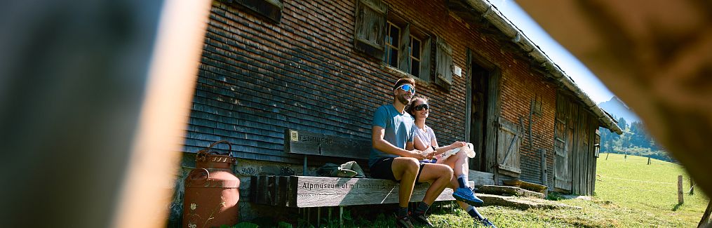 Two people are sitting on the bench in front of the Alpine Museum on the Tannberg.