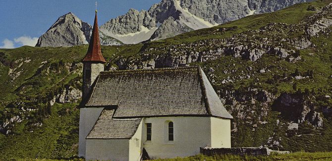 An old photograph of the Simmel Chapel in summer, with a mountain range in the background.