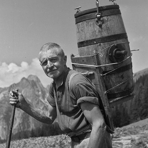 Historic photo of a man carrying a wooden barrel on his back.