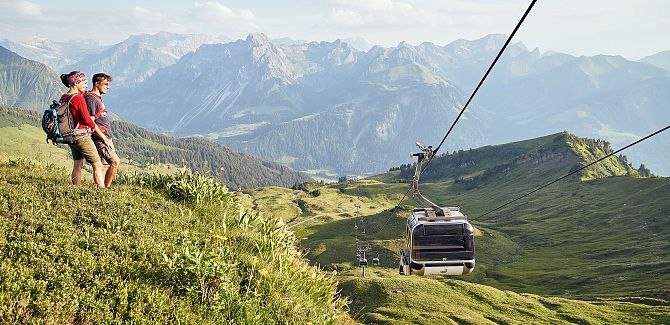 Two people are standing on a hill and looking at the moving Didamskopfbahn.
