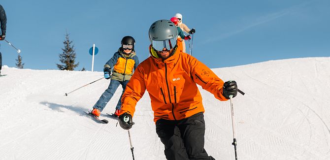 Kinder fahren hinter einem Skiguide her.