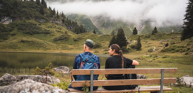 Zwei Personen sitzen auf einer Bank am Körbersee, während Nebel die Landschaft verhüllt.