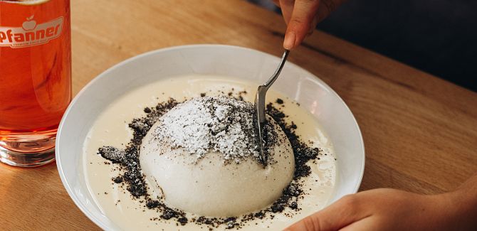 A Germknödel with vanilla sauce and poppy seeds is being eaten, accompanied by a Skiwasser drink.