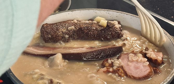 Gerstensuppe wird gerade umgerührt, darin ist Speck zu sehen.
