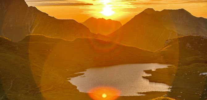 Hochalpsee lies peacefully, while behind it the sky glows in a vibrant orange from the sunset.