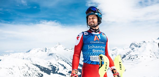 Johannes Strolz steht im Rennanzug, hinter ihm die verschneiten Berge.