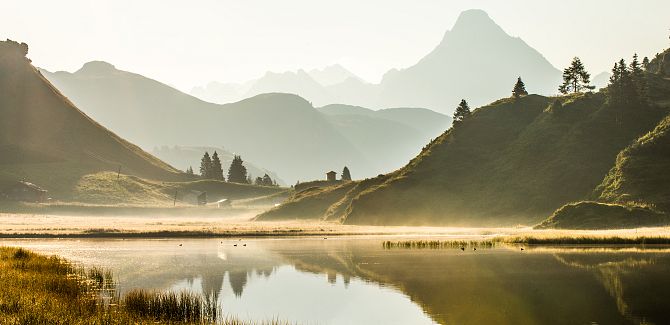 Der Kalbelesee liegt eingebettet in eine farbenfrohe Herbstlandschaft, im Hintergrund ragt der Biberkopf empor.