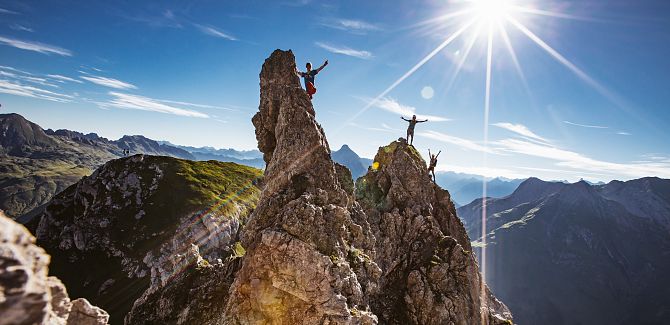 Three people climb the Karhorn via ferrata, with a clear blue sky stretching out behind them.