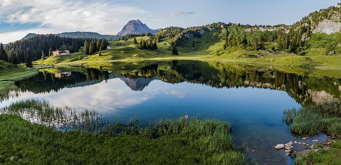 View of Körbersee with the Berghotel Körbersee on the shore, and the Widderstein rising in the background, its reflection mirrored in the water.
