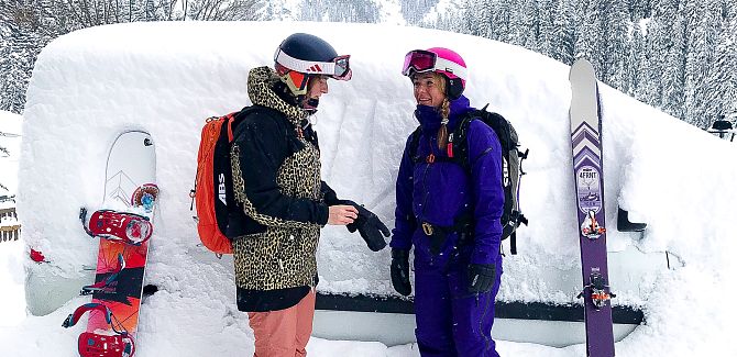 Two women stand in front of their snow-covered car.