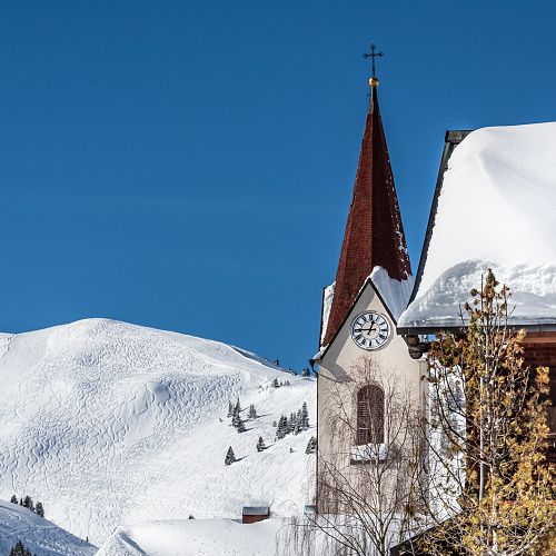 Church tower of Warth, with the Wiltrud house in front and the ski slope behind.