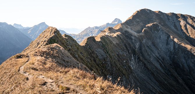 A mountain ridge in autumnal hues, with further mountain ranges in the background.