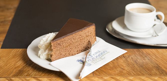 A Sachertorte is served with cream and a cup of coffee.