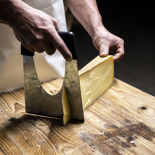 A man is cutting a slice of mountain cheese with a cheese knife.