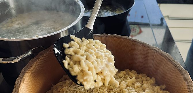 Knödel werden gerade aus dem Kochwasser in eine Holzschüssel geschöpft.