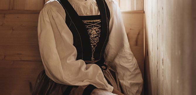 Eine Frau in traditioneller Walsertracht sitzt vor einer Holzwand.
