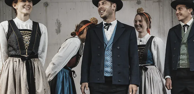 Ladies and gentlemen in traditional Walser costume standing in front of a concrete wall.