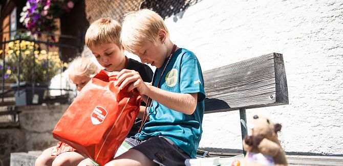 Drei Kinder packen ihre Belohnung vom Murmele-Pass aus.