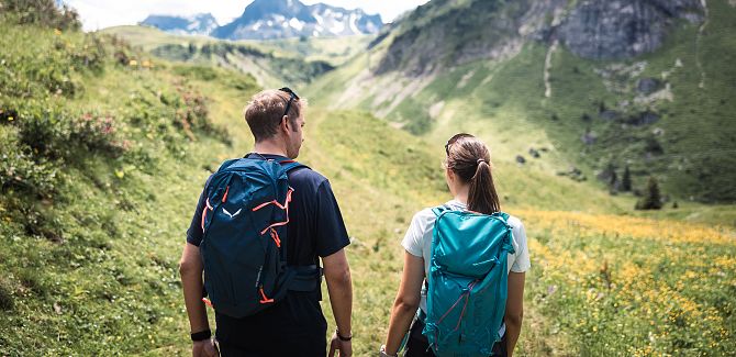 A couple is hiking together through green meadows.
