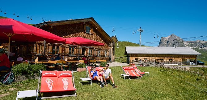 The sun terrace of the Hochalphütte is equipped with red parasols and deck chairs.