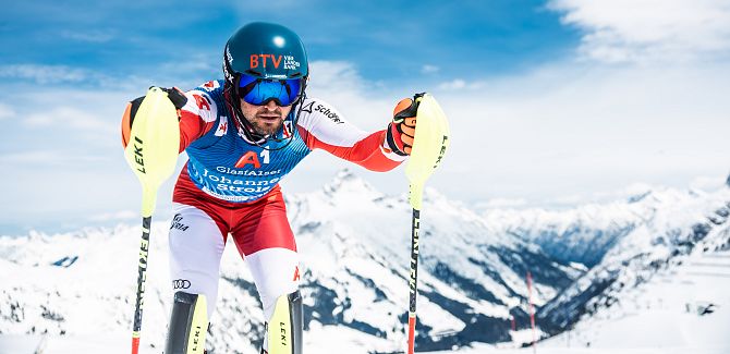 Johannes Strolz gets ready for the descent, with snow-covered mountains rising behind him.