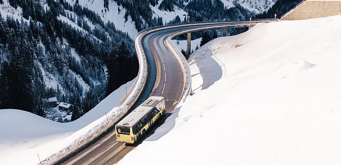 A yellow bus is approaching a curved bridge, surrounded by a snow-covered landscape.