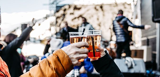 Two people toast with Aperol as the band performs in front of them at Ski & Concert.