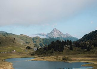 A lady stands on the shore of Lake Kalbele and gazes at the Biberkopf. The autumn landscape spreads out around her in vibrant colors.