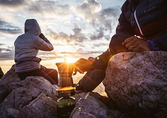 At the summit of Widderstein, two people make themselves a hot coffee and enjoy the view.