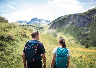 A couple is hiking together through green meadows.